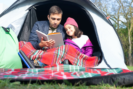 father and daughter reading a book inside tent