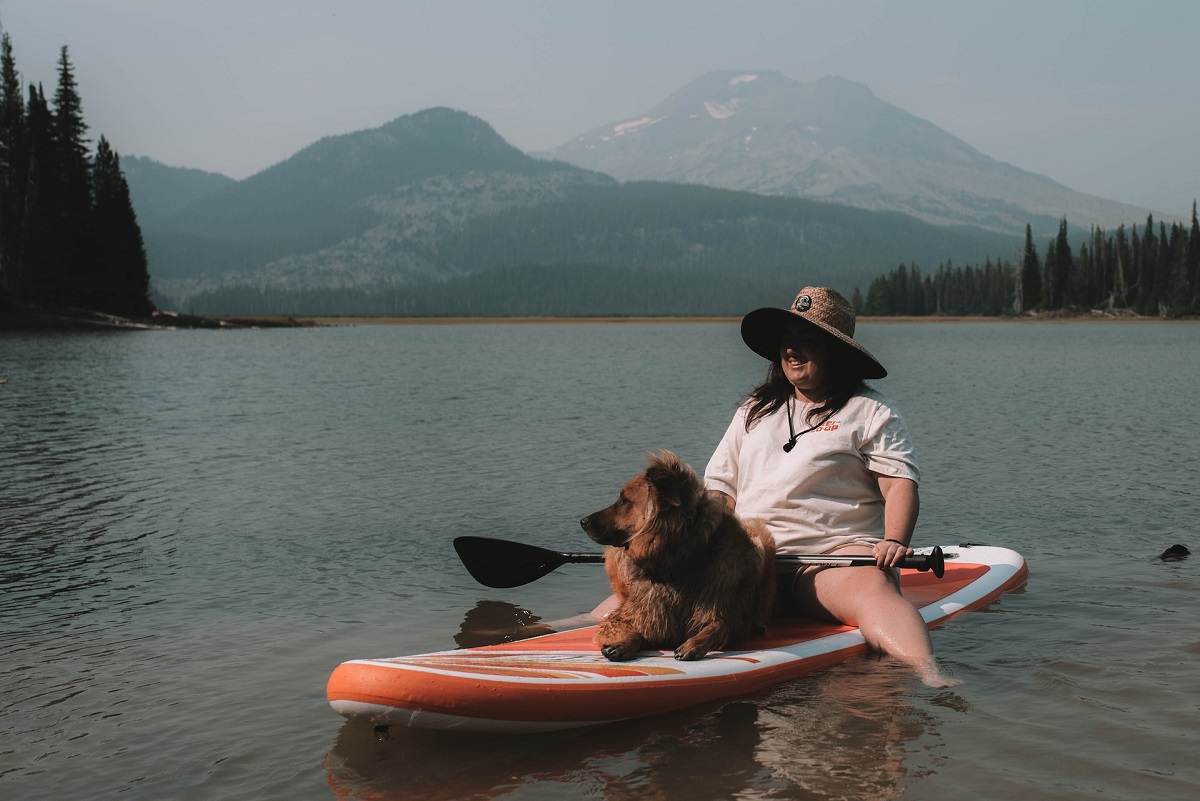 A woman and her dog paddleboarding on a lake.