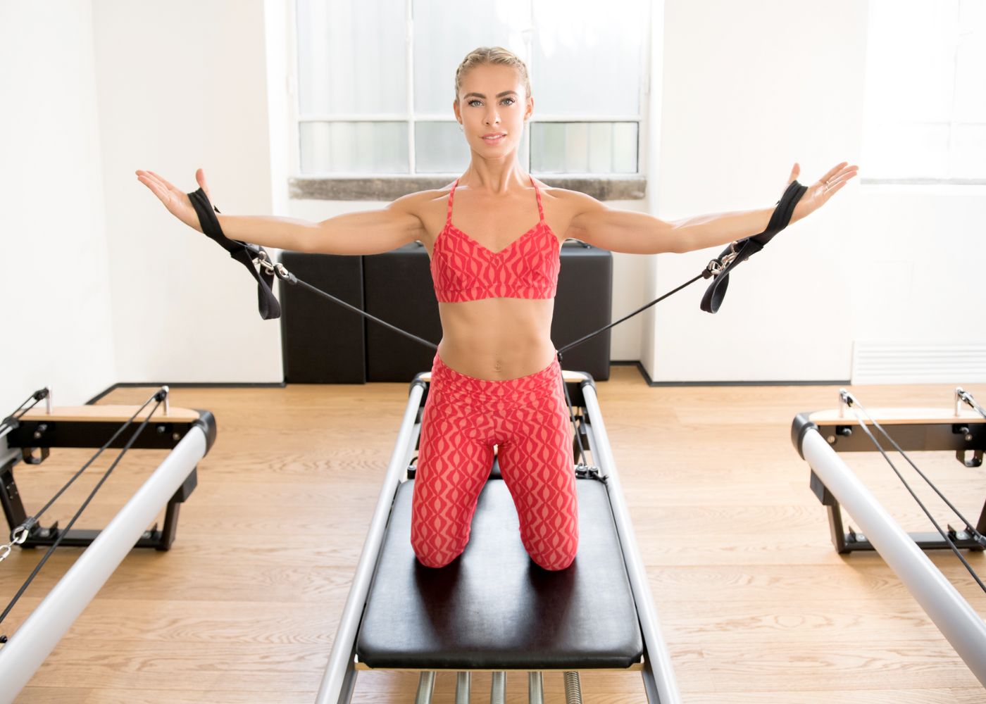women on home Pilates reformer working her arms with hands in short straps out in fly position